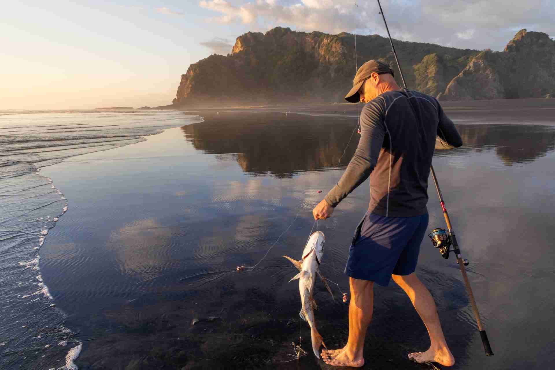 Angler walking along a New Zealand west coast beach at sunrise holding a freshly caught fish