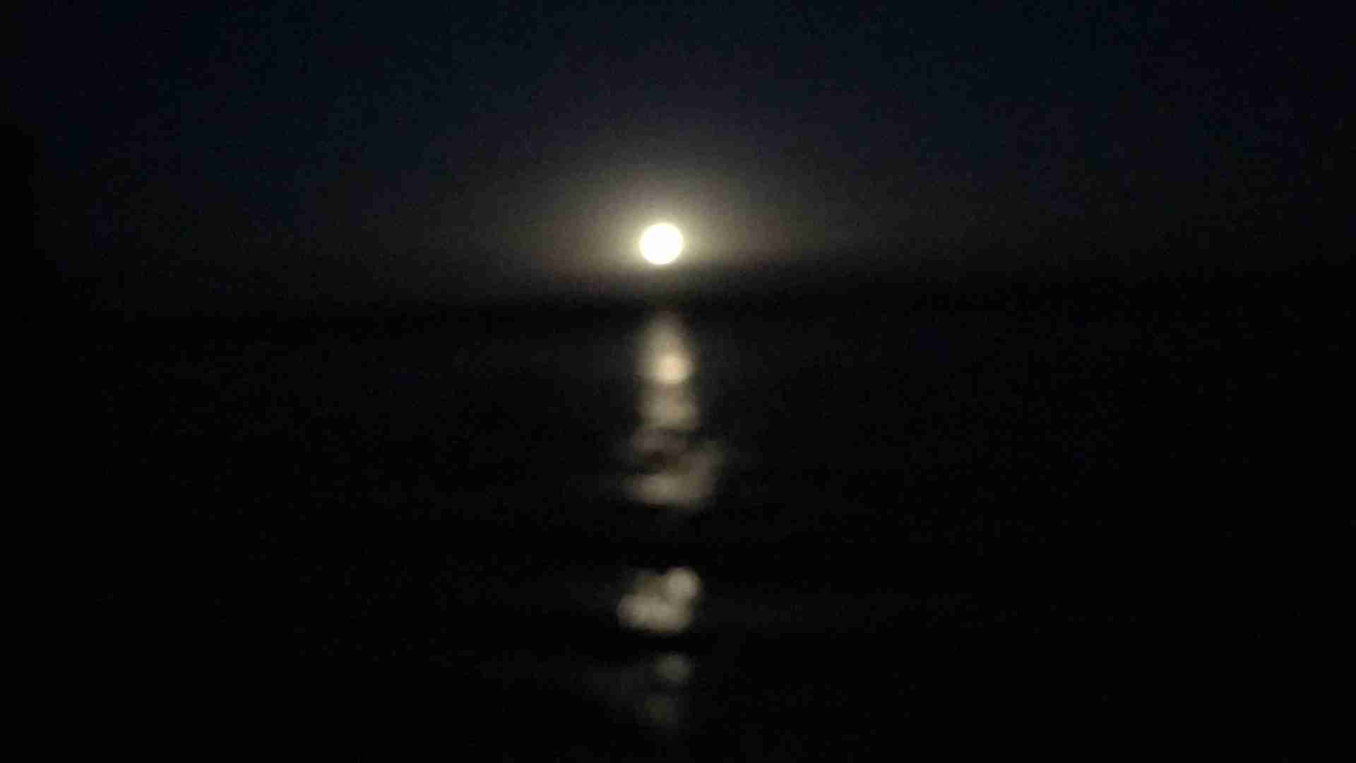 Full moon rising over the horizon, reflected in calm water at sea