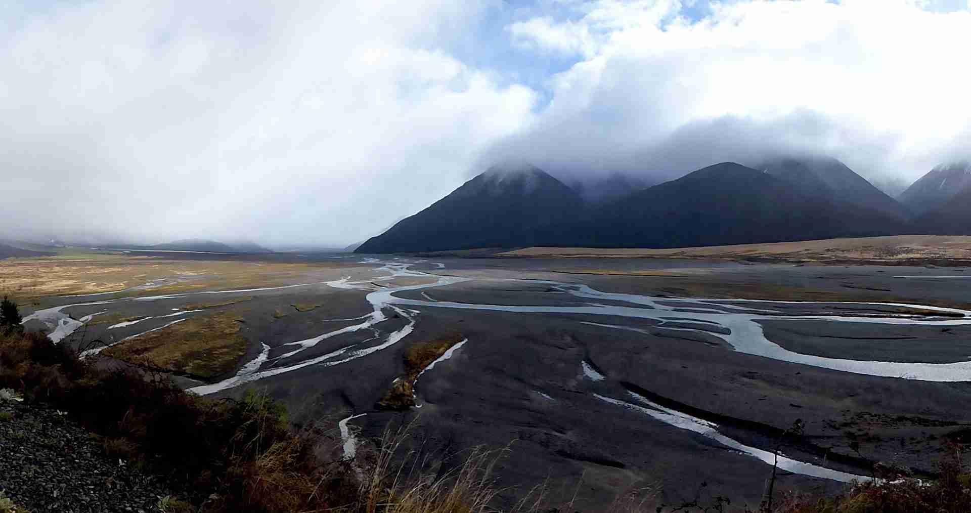 A braided river winding in multiple channels across the Canterbury plains and farmland under an open sky
