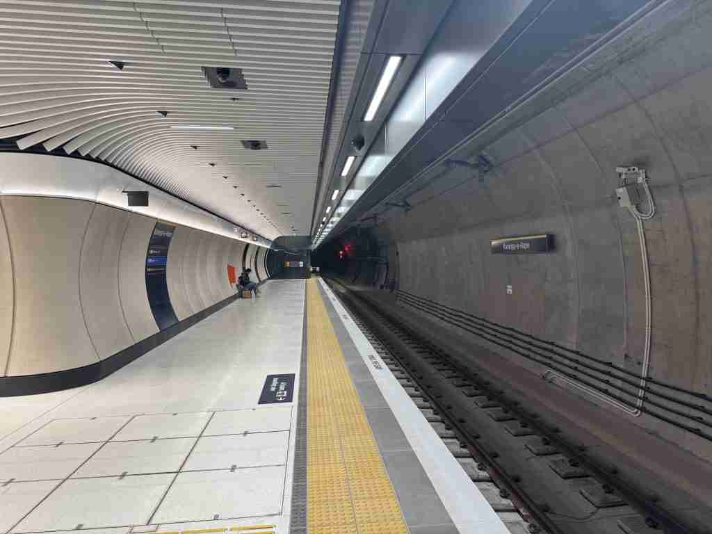 Karanga-a-Hape Station platform with the bored tunnel wall and station name sign, and one passenger seated